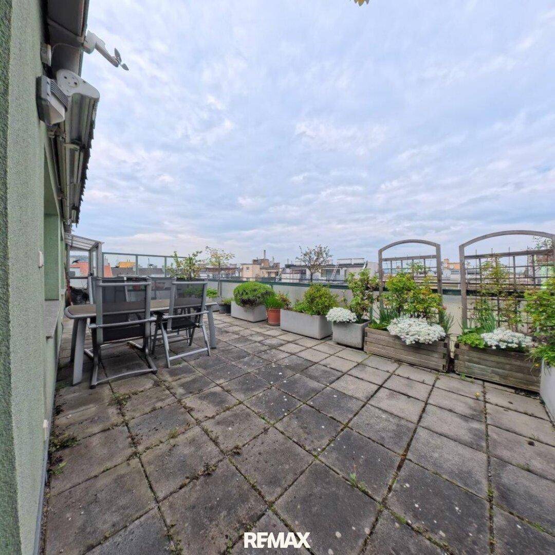 Geräumige Dachterrasse mit Pflastersteinen, Gartenmöbeln und Pflanzen unter weitem Himmel.