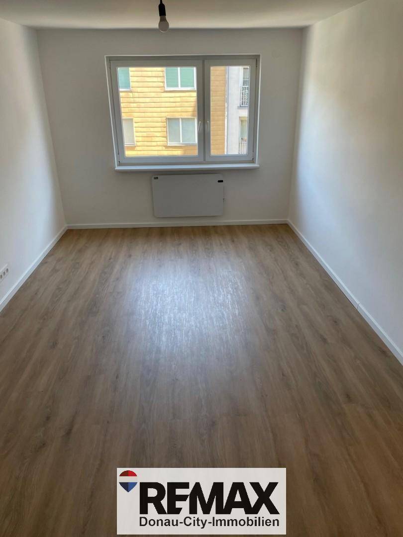 Geräumiger, heller Raum mit Laminatboden und großen Fenstern, ideal als Wohn- oder Schlafzimmer nutzbar.