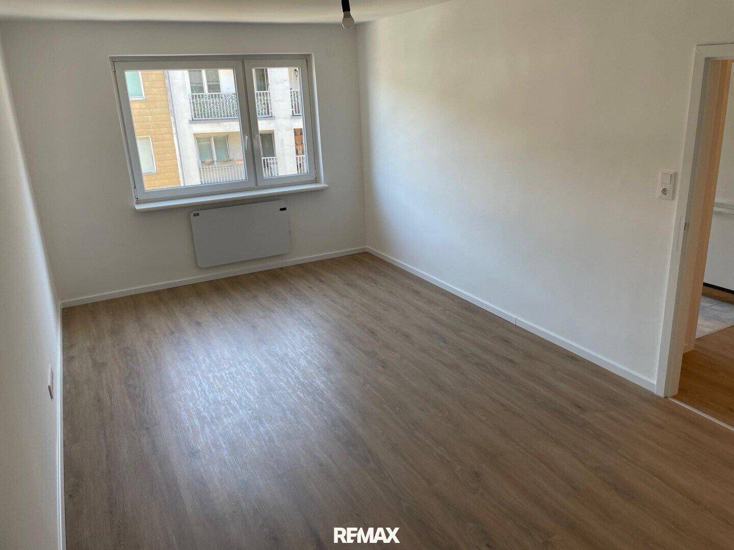 Heller, leerer Raum mit Laminatboden, weißen Wänden und einem Fenster mit Blick auf die Umgebung.
