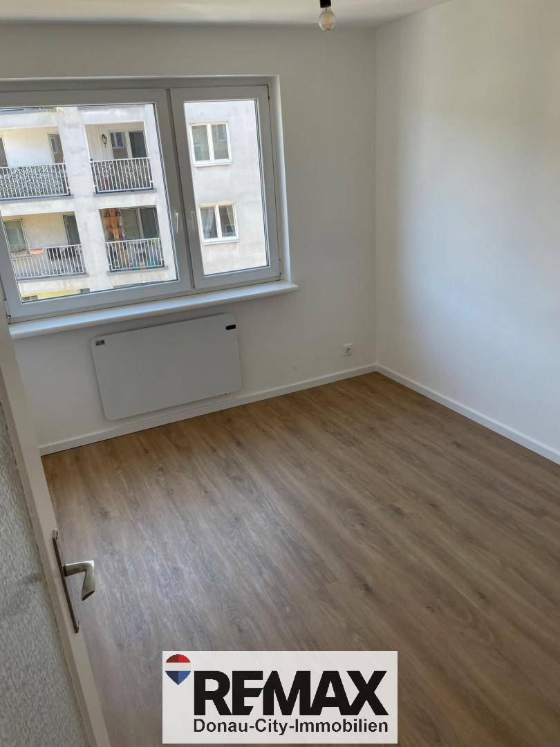 Lichtdurchfluteter Raum mit hellem Laminatboden und einem Fenster, das viel Tageslicht hereinlässt.