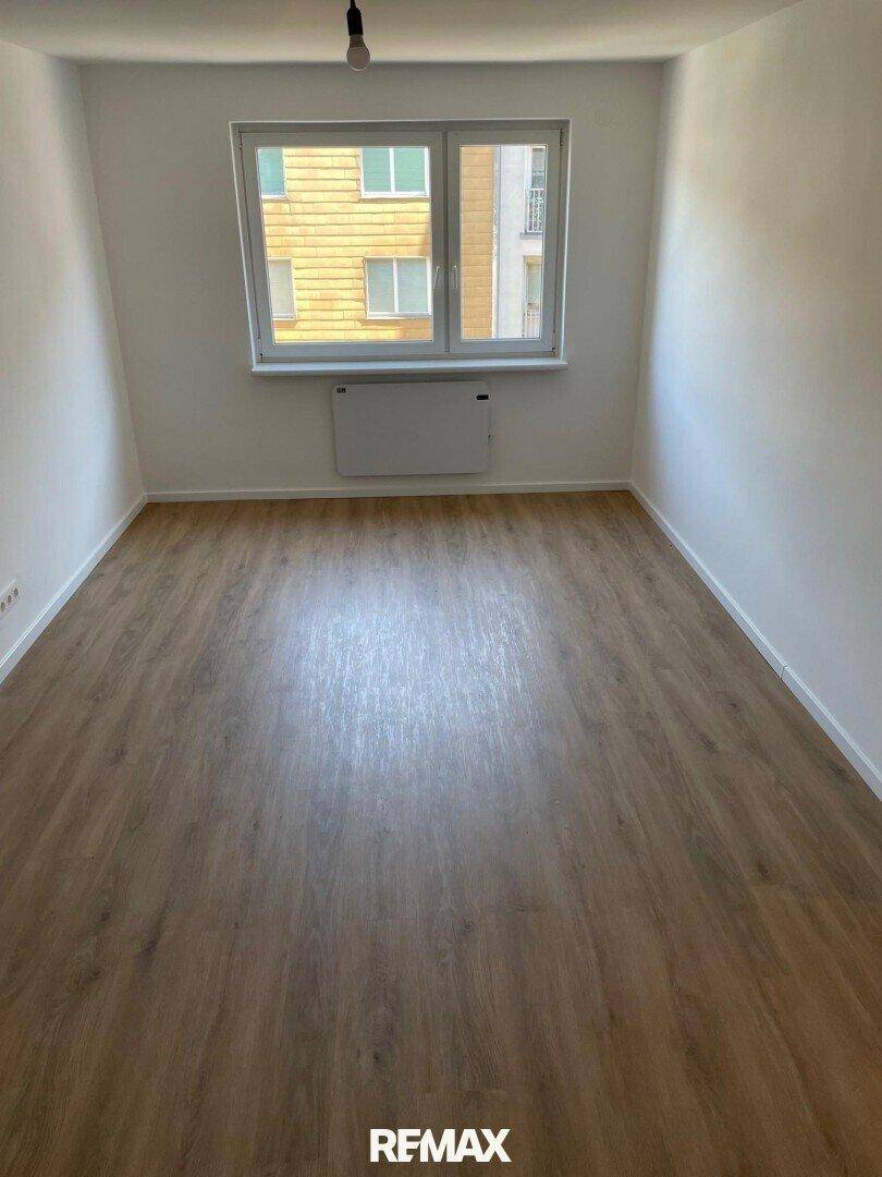 Geräumiger, unmöblierter Raum mit hellem Laminatboden und großen Fenstern, die viel Tageslicht hereinlassen.