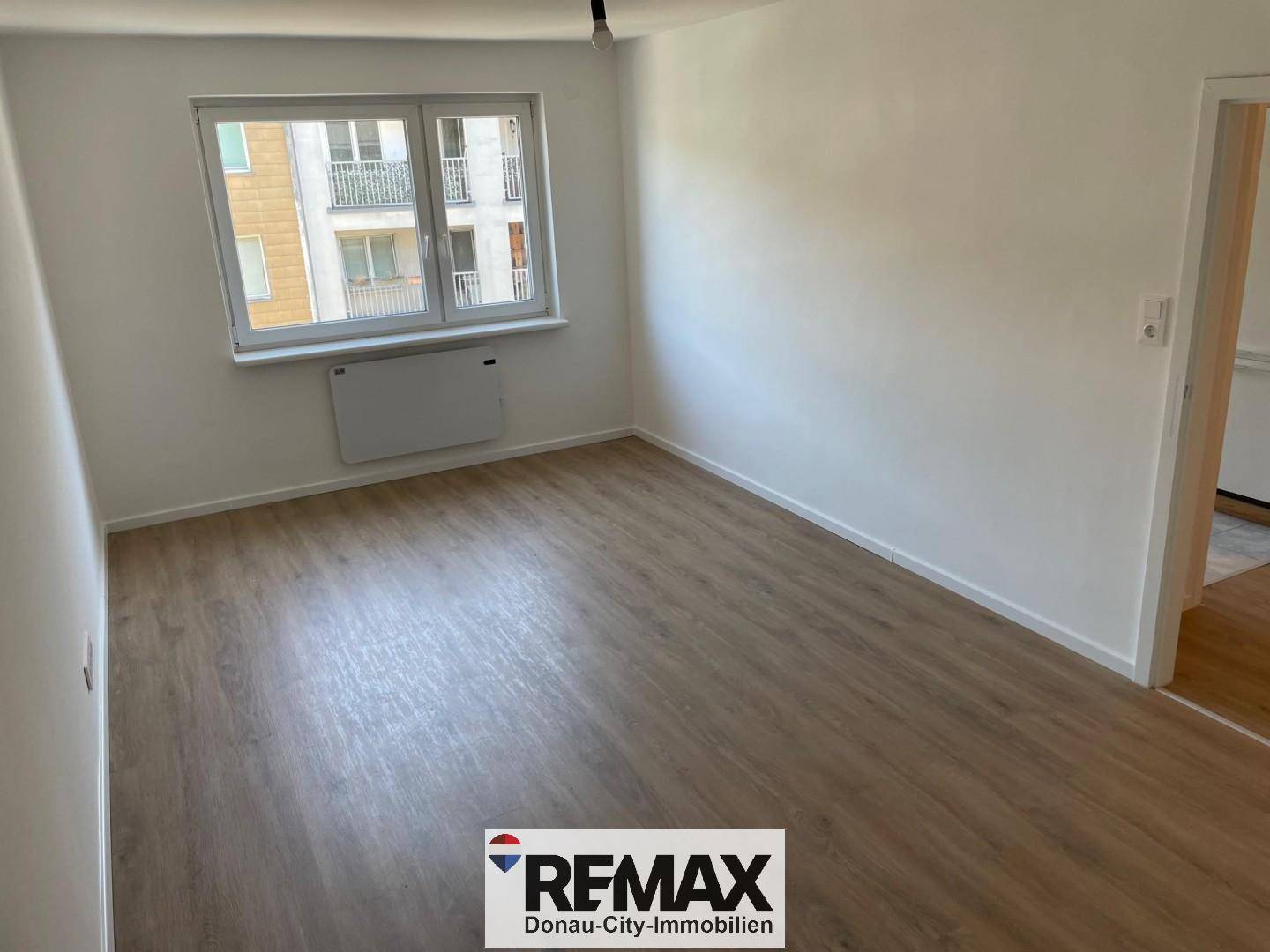 Heller, leerer Raum mit modernem Laminatboden, weißen Wänden und Blick auf umliegende Gebäude.