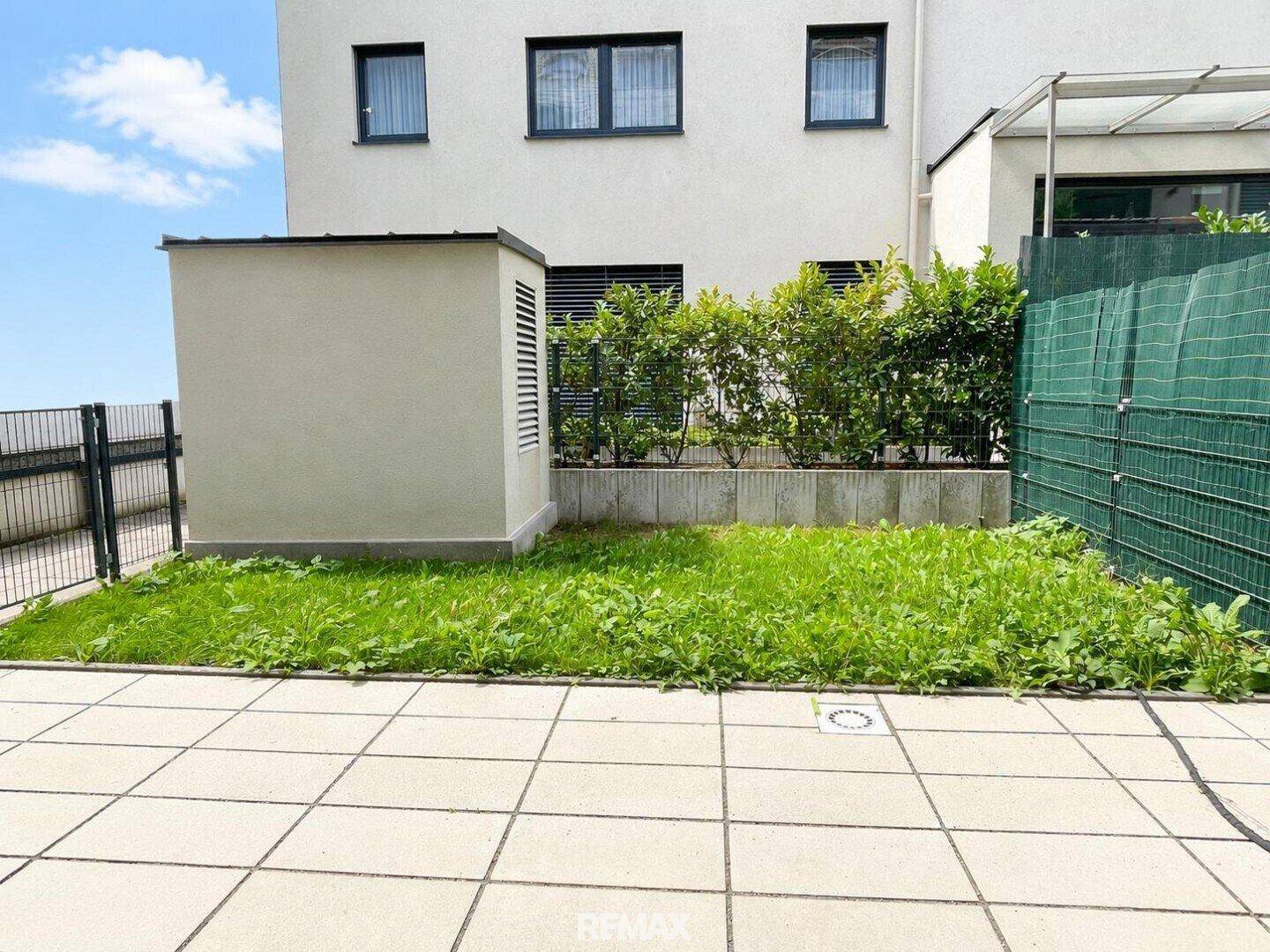Kleiner Gartenbereich mit gepflasterter Terrasse und Rasenfläche hinter dem Gebäude.