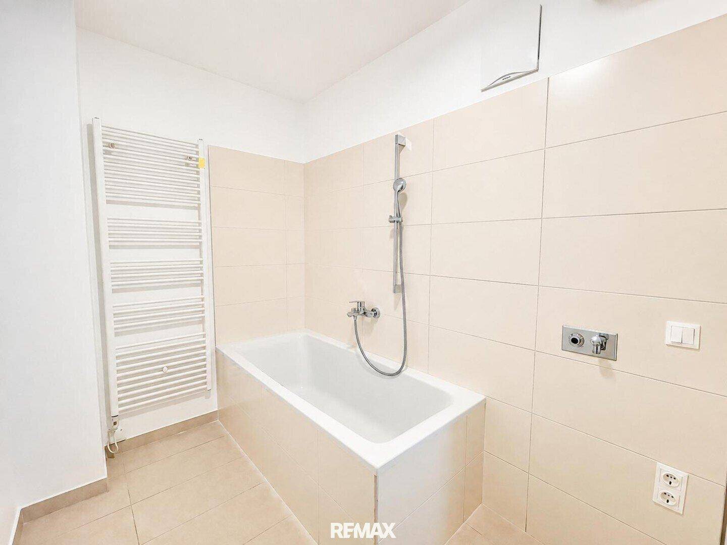 Badezimmer mit Badewanne und beheiztem Handtuchhalter, ausgestattet mit hellen Fliesen.