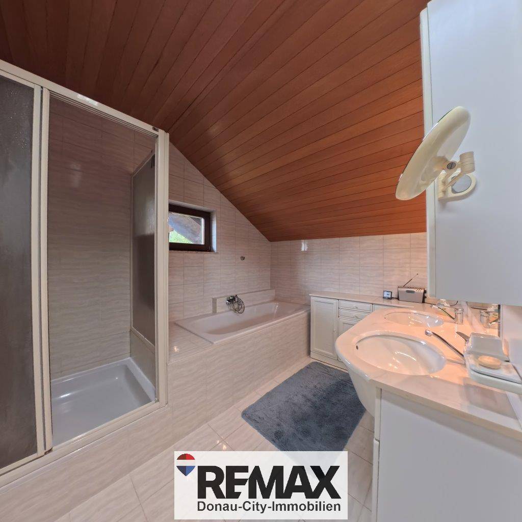 Dachgeschoss-Badezimmer mit Holzdecke, Badewanne, Duschkabine und Waschbecken.