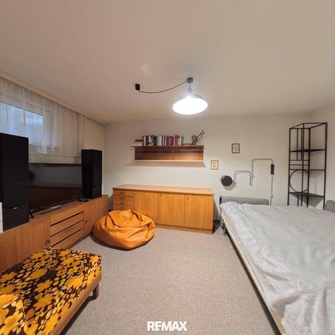 Helles Zimmer mit Bett, Holzmöbeln, einem orangefarbenen Sitzsack und Teppichboden.