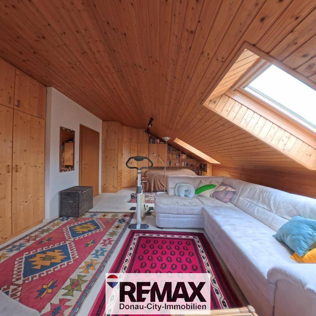 Gemütlicher Dachboden-Wohnbereich mit Holzverkleidung, großem Sofa und Dachfenster.