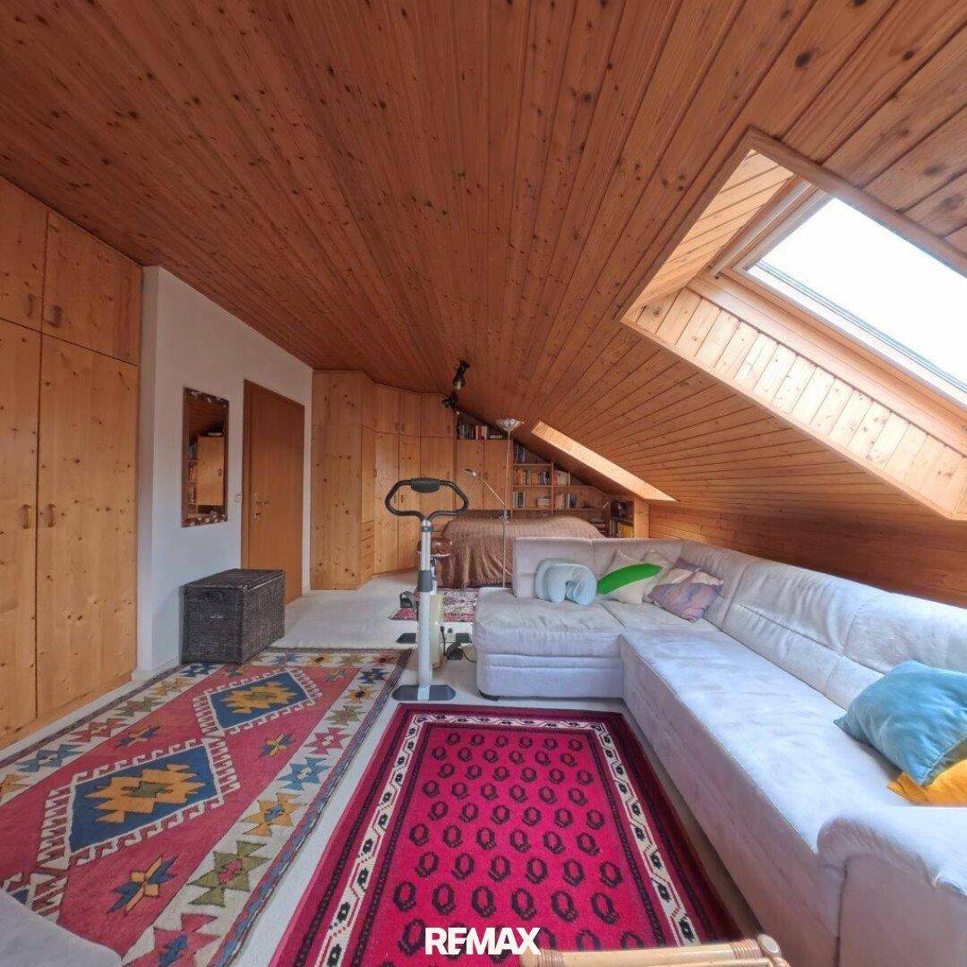 Gemütlicher Dachboden-Wohnbereich mit Holzverkleidung, Dachfenster und bequemer Sitzecke.