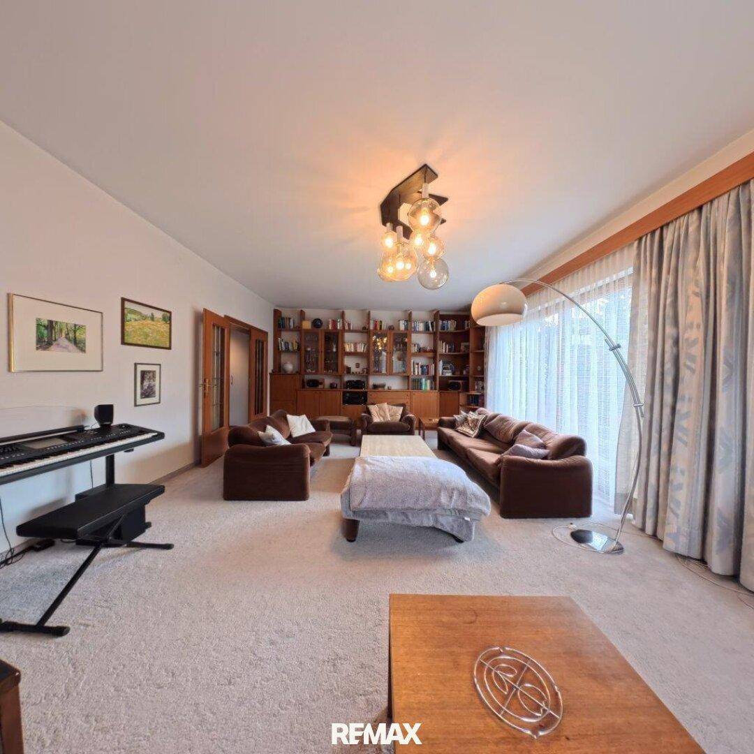 Gemütliches Wohnzimmer mit Teppichboden, bequemen Sofas und einem Klavier, hell durch große Fenster.