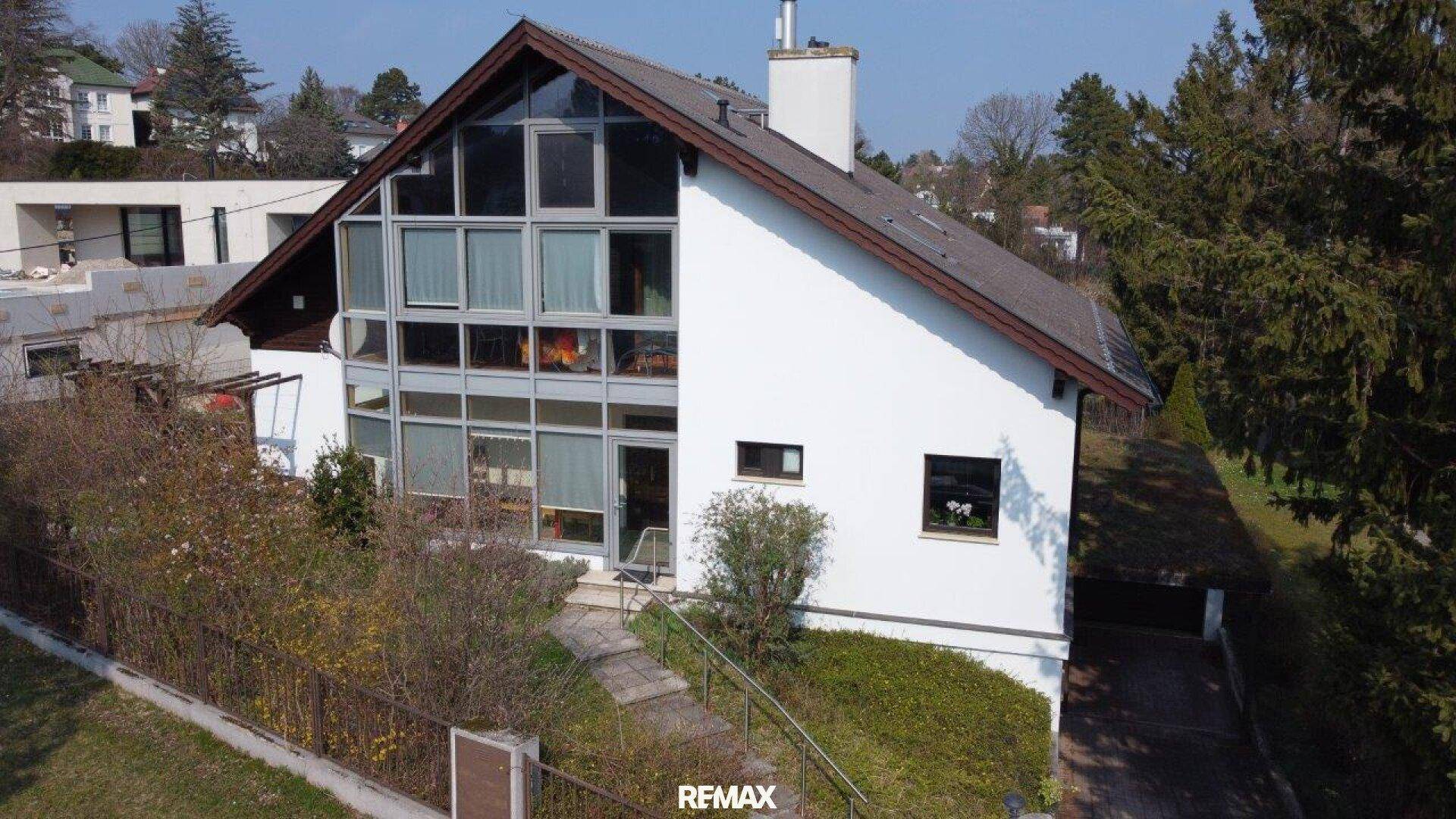 Ansicht des Hauses mit markanter Glasfassade und Satteldach, eingebettet in eine grüne Umgebung.