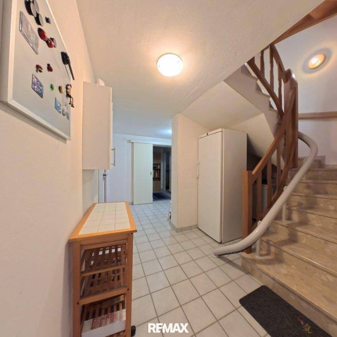 Heller Flur mit Fliesenboden, einem Kühlschrank und einer Treppe, die die Etagen verbindet.