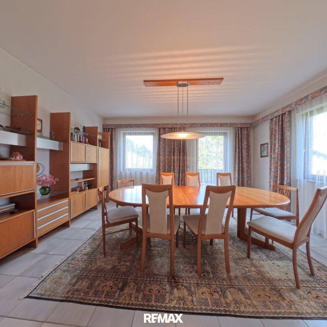 Geräumiges Esszimmer mit großem ovalen Holztisch, passenden Stühlen und eleganten Vitrinen.