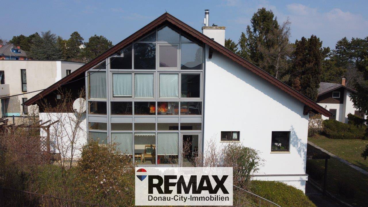 Architektonisch ansprechendes Haus mit großer Glasfront und weißer Fassade, eingebettet in die Landschaft.