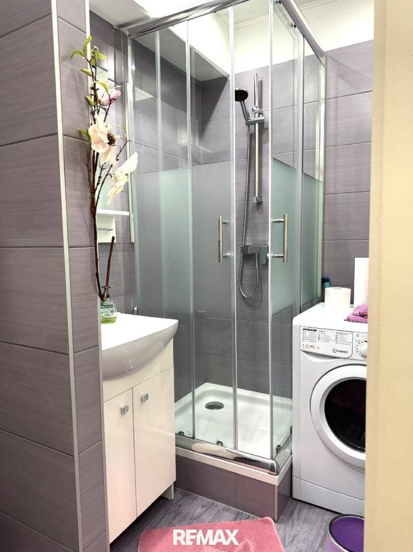 Badezimmer mit Duschkabine, Waschbecken und Waschmaschine.