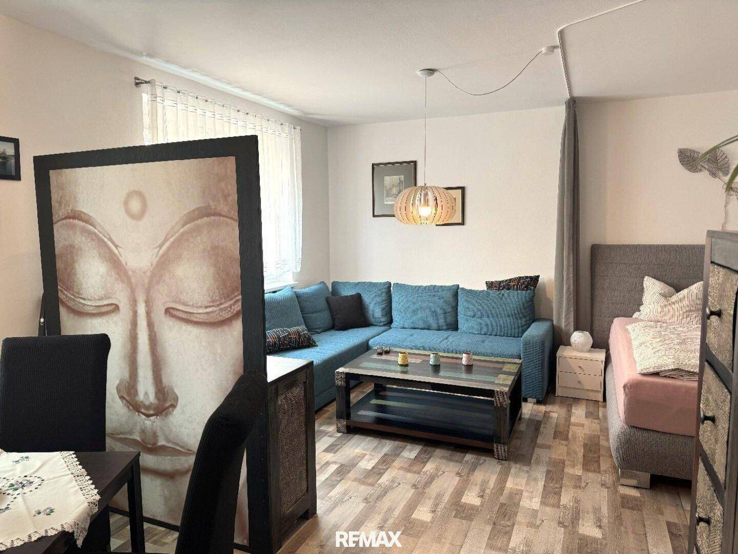 Heller Wohnbereich mit blauem Ecksofa, Couchtisch und dekorativem Buddha-Bild.