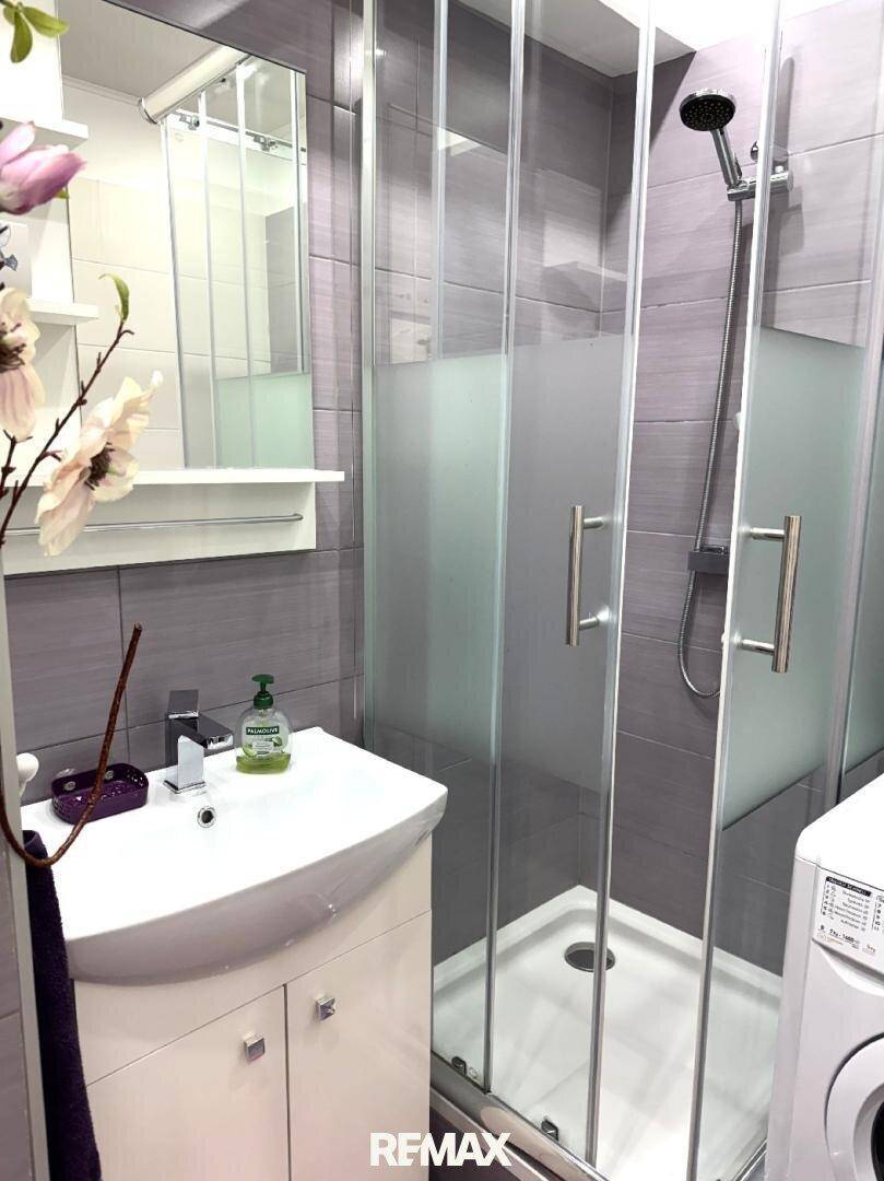 Modernes Badezimmer mit Duschkabine, Waschbecken und grauen Fliesen.
