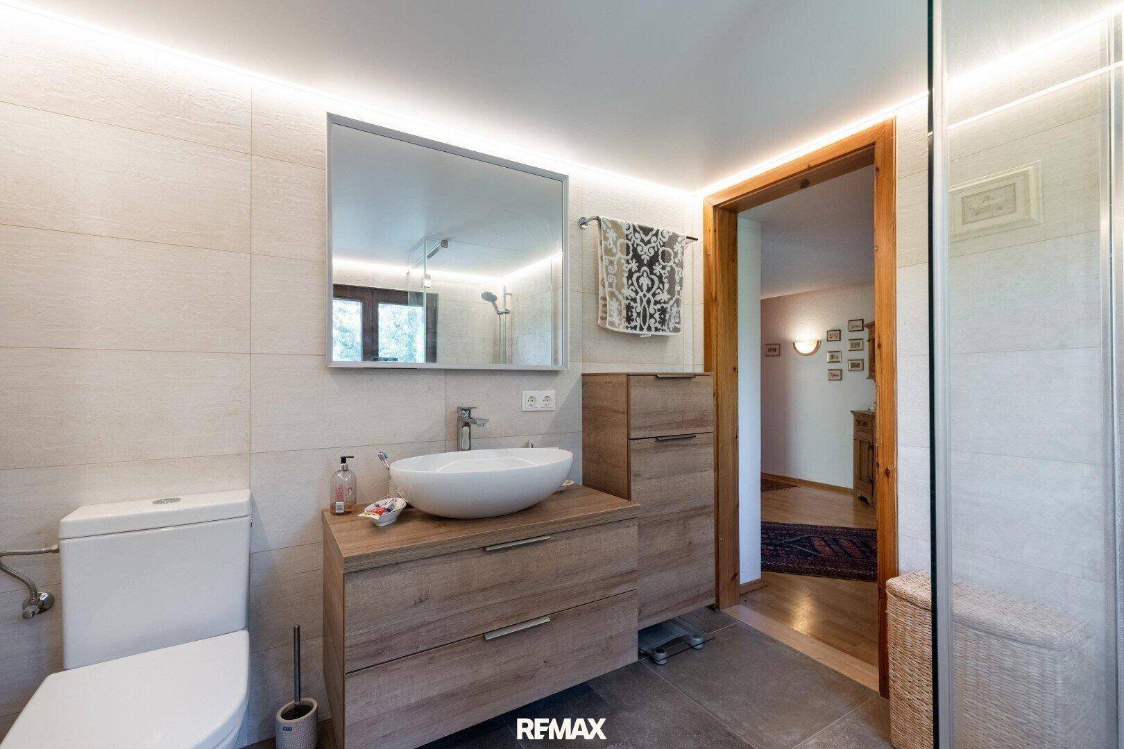 Funktionales Badezimmer mit Waschtisch, WC und Zugang zu einem Flur mit Holztüren.