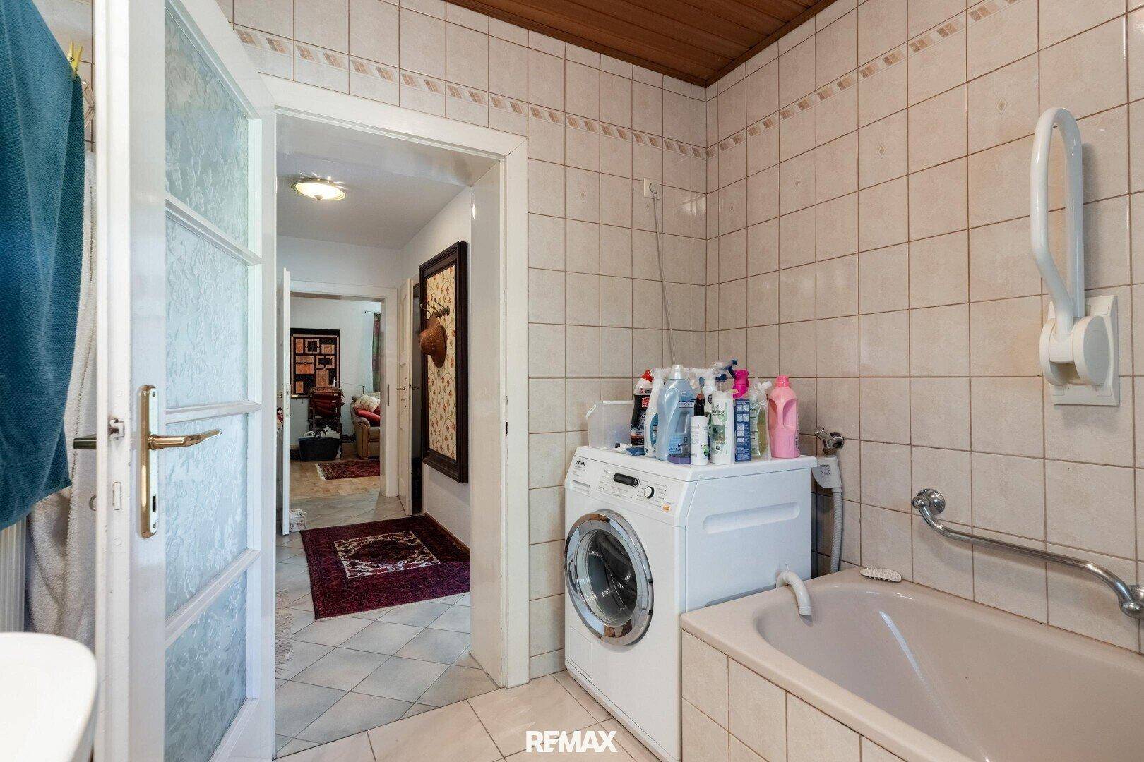 Funktionales Badezimmer mit Badewanne, Waschmaschine und Fliesenboden.