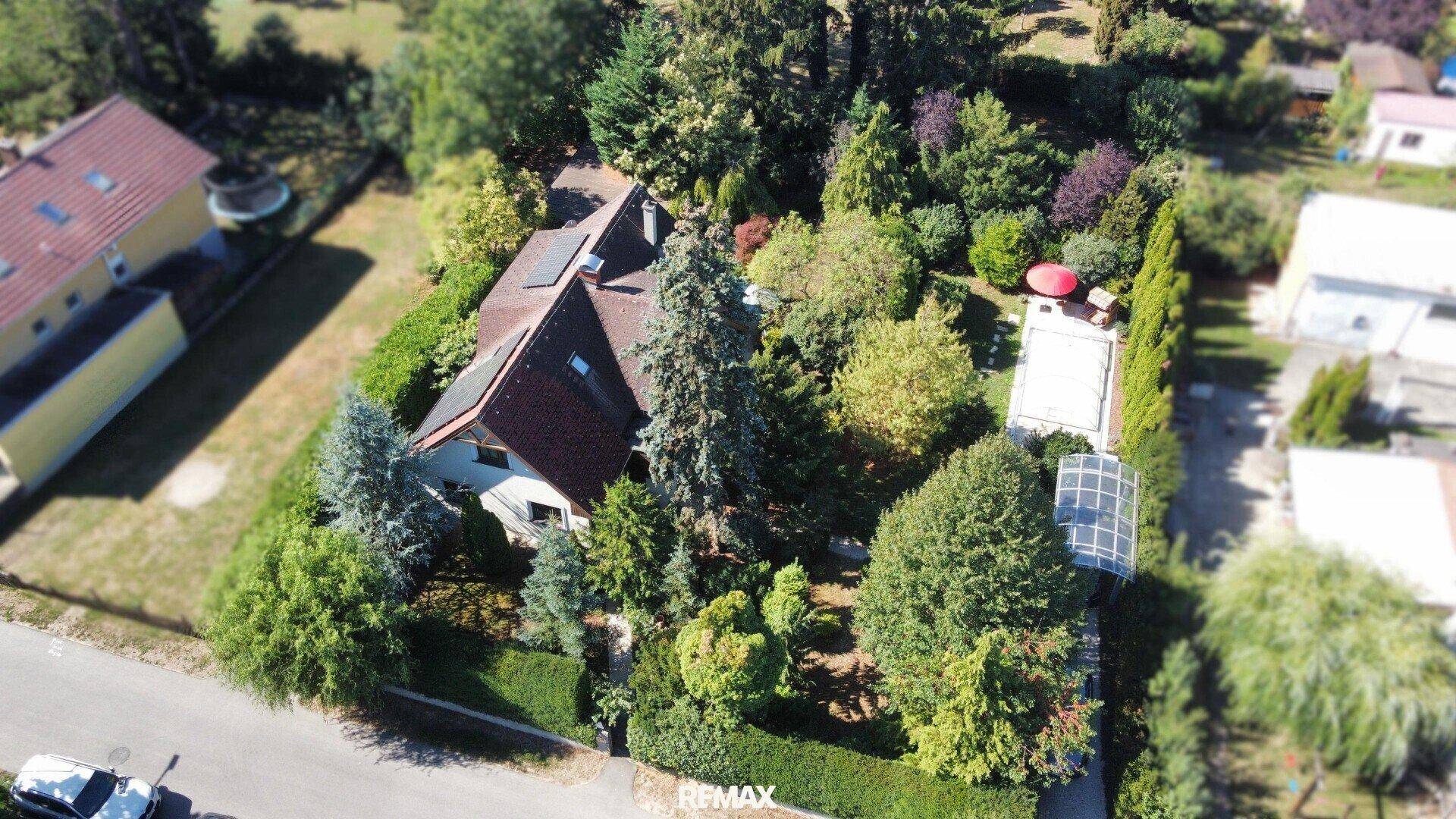 Luftaufnahme eines Wohnhauses mit großem Garten, Bäumen, Photovoltaikanlage und Poolbereich.
