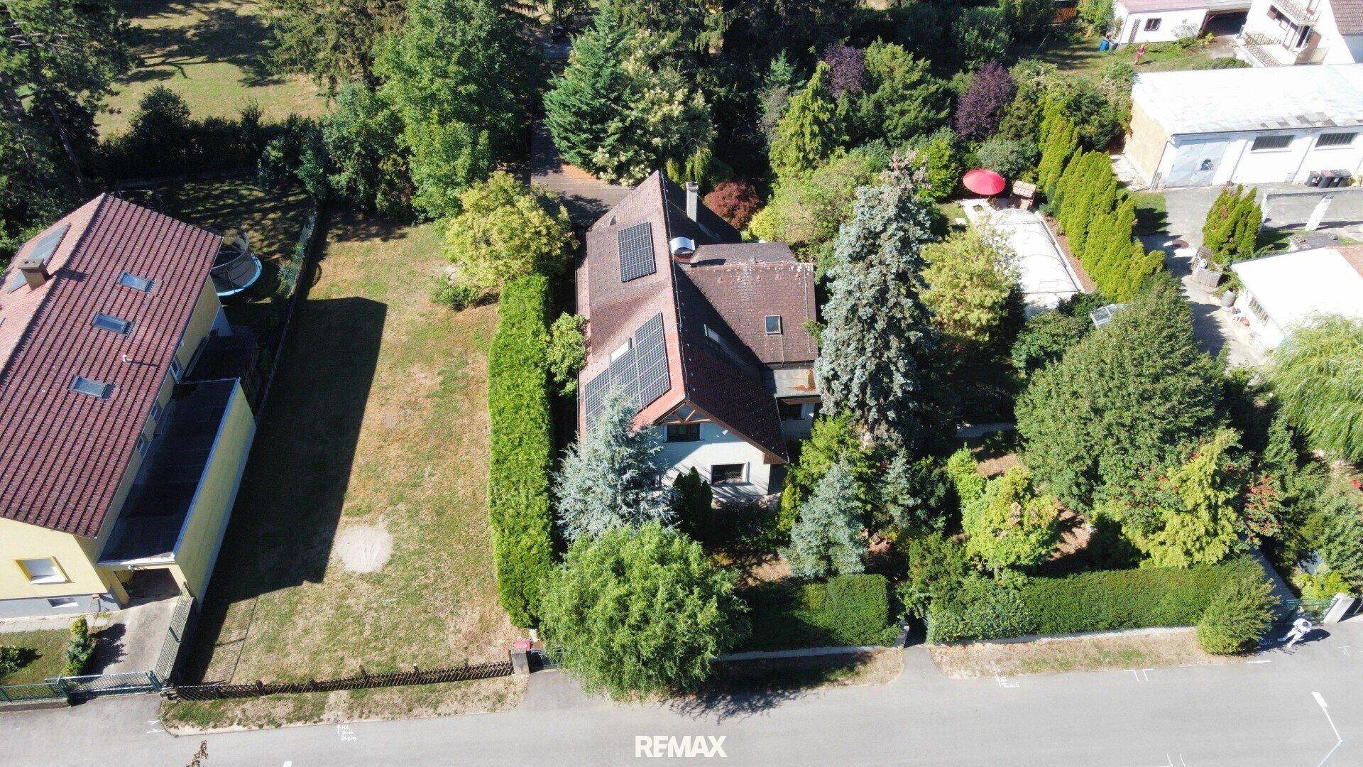 Luftaufnahme eines Wohnhauses mit großem Garten, Bäumen und Photovoltaikanlage auf dem Dach.