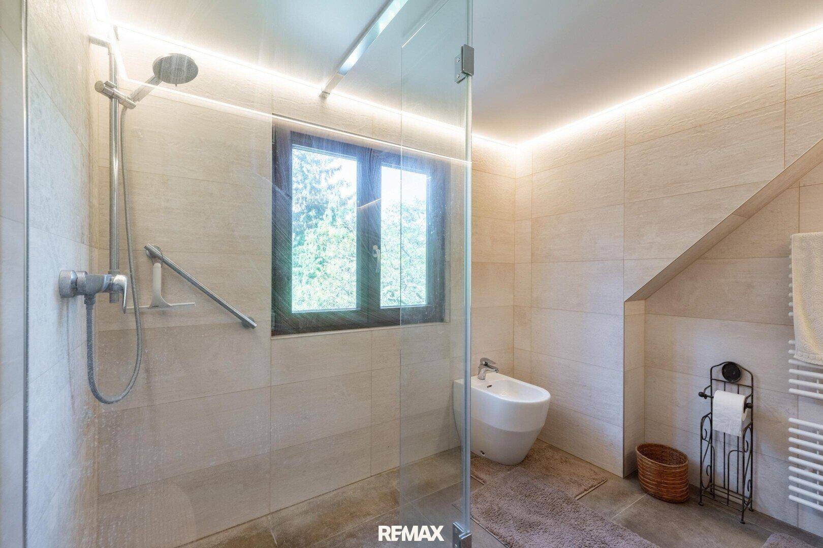 Modernes Badezimmer mit begehbarer Dusche, Bidet, Fenster und schrägen Wänden unter dem Dach.