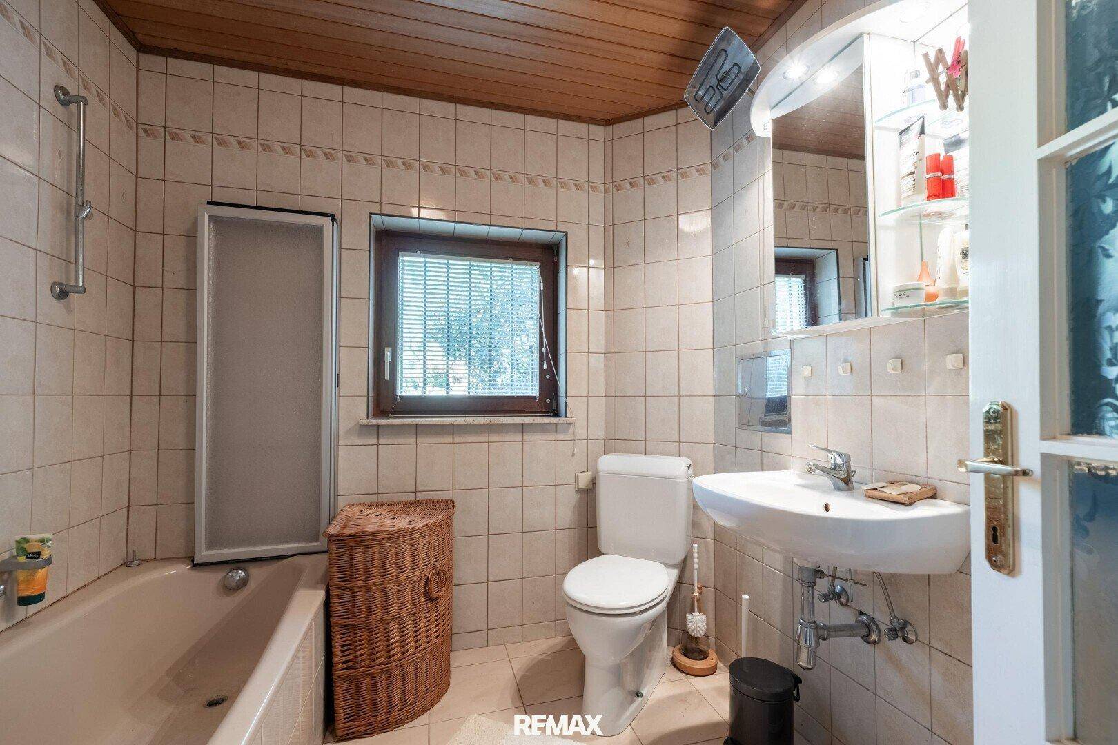 Gefliestes Badezimmer mit Badewanne, WC, Waschbecken und Holzdecke.