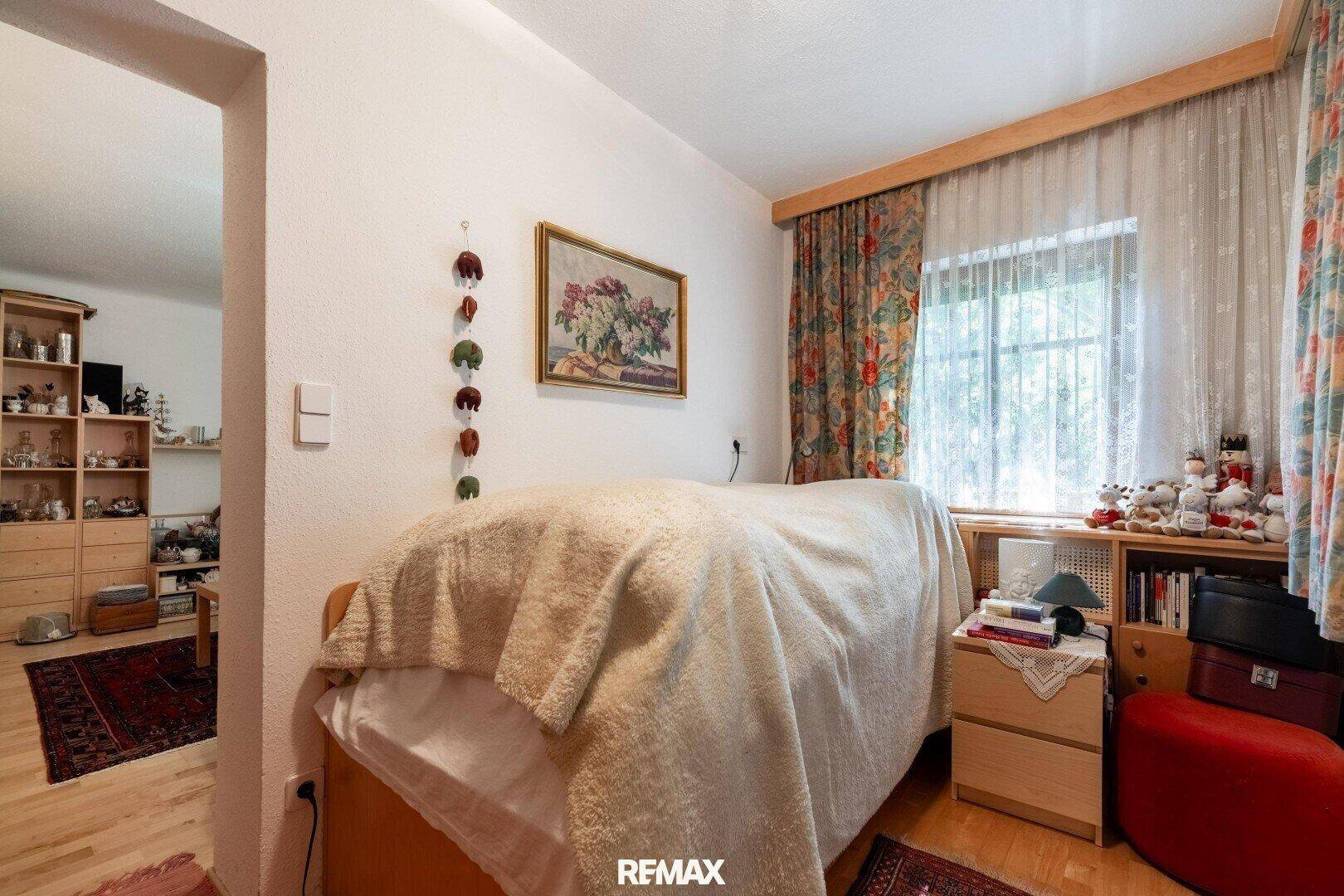 Gemütliches Schlafzimmer mit Holzboden, großem Fenster und Blick in einen angrenzenden Raum.