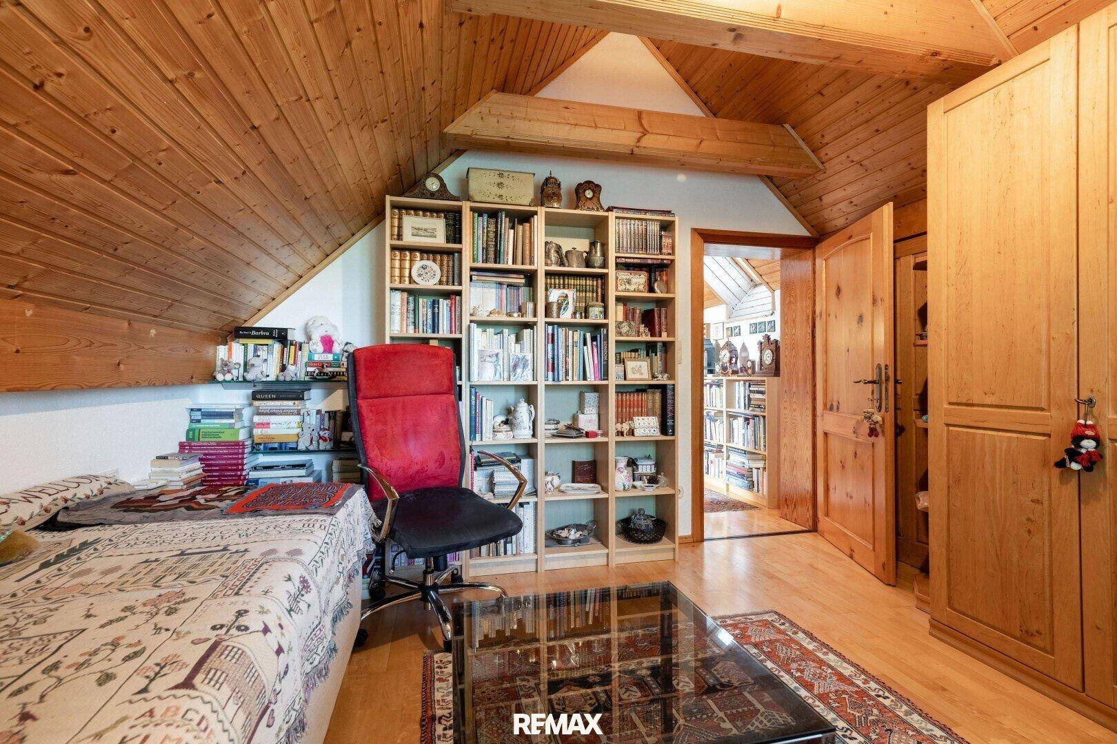Geräumiges Schlafzimmer im Dachgeschoss mit Holzdecke, Bücherregalen und gemütlicher Einrichtung.