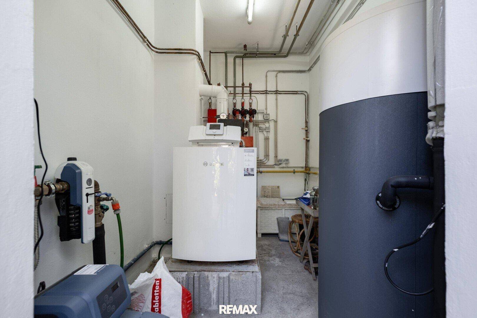 Technikraum mit Warmwasserspeicher, Heizungsanlage und sichtbaren Rohrleitungen.