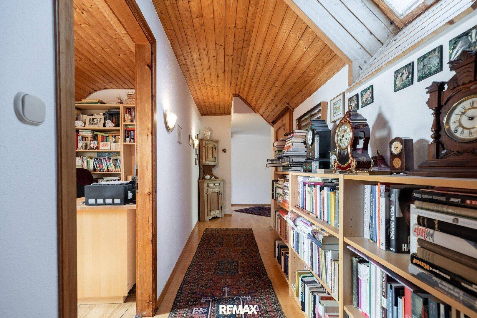 Heller Flur im Dachgeschoss mit Holzdecke, Bücherregalen und Zugang zu weiteren Räumen.