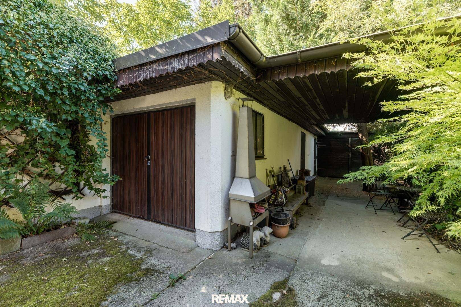 Außenansicht der Garage mit Holztoren, einem Grillplatz und gepflastertem Vorbereich.