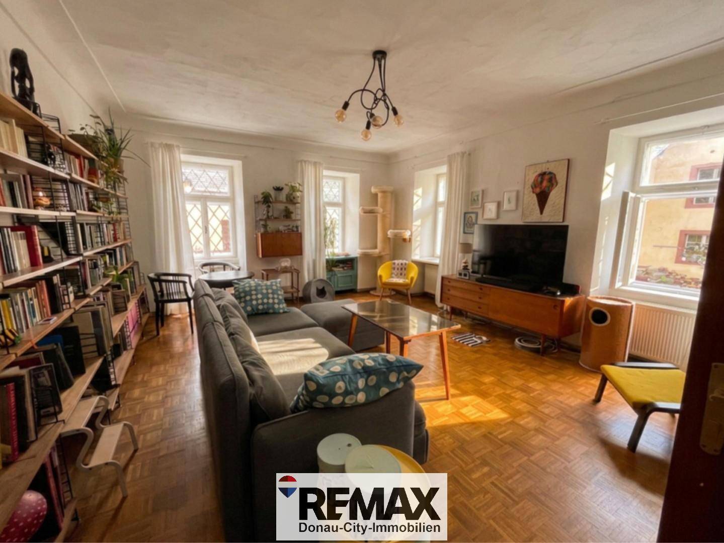 Gemütliches Wohnzimmer mit Bücherregal, Parkettboden und mehreren Fenstern für viel Tageslicht.