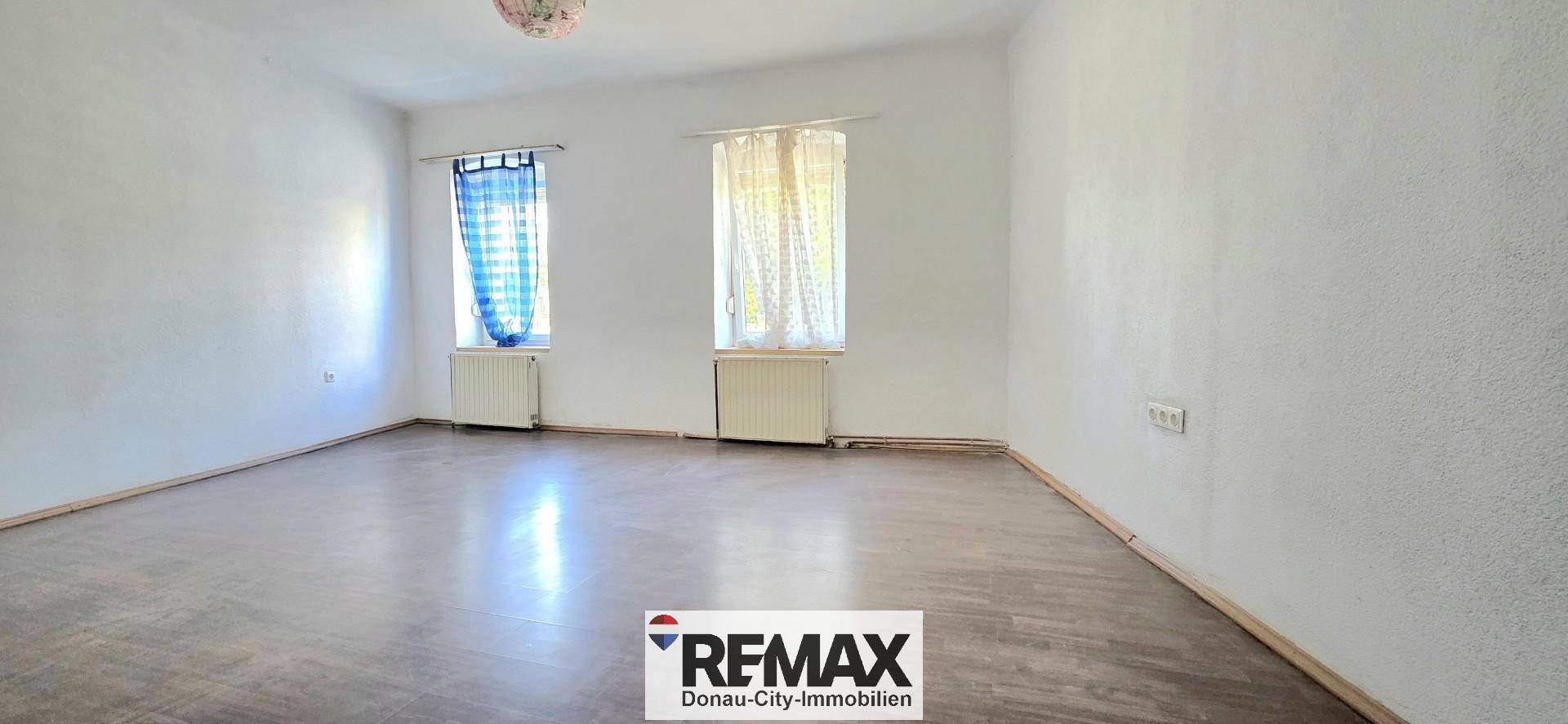 Geräumiges, helles Zimmer mit Holzfußboden, zwei Fenstern und Heizkörpern.