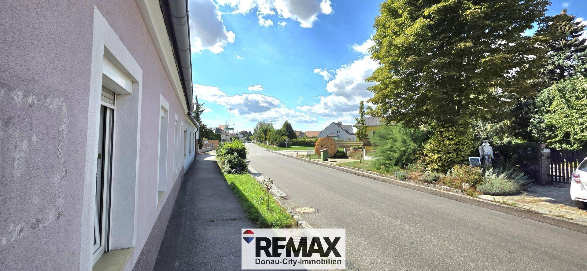 Seitenansicht des Hauses entlang der ruhigen Straße mit Bäumen und Grünflächen.