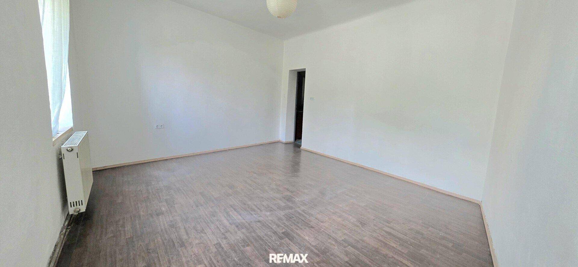 Leeres Schlafzimmer mit Holzfußboden, weißen Wänden und einem Fenster.