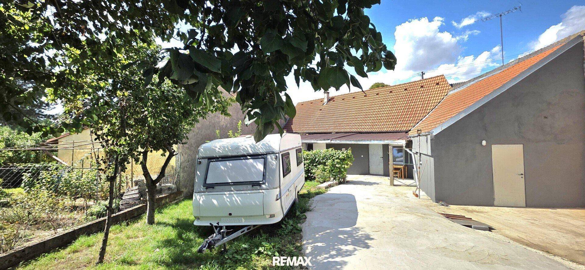 Seitenansicht des Hauses mit einem Wohnwagen im Gartenbereich und Bäumen.