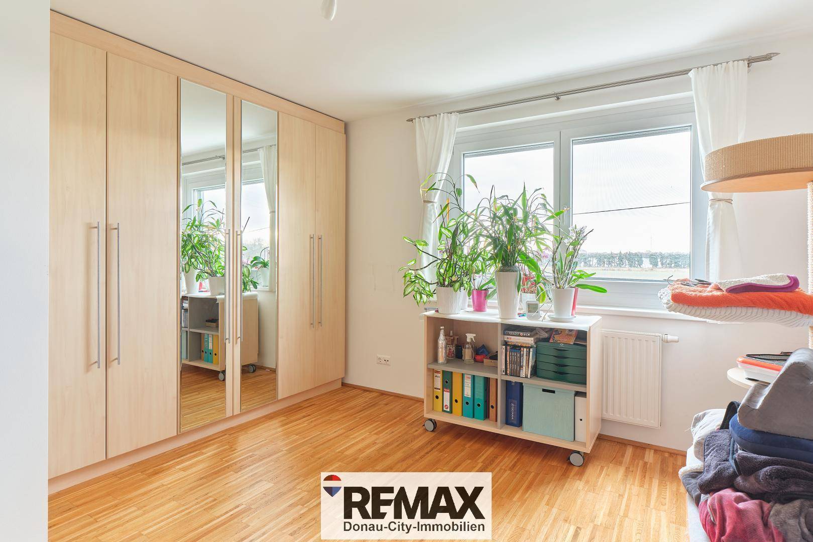 Schlafzimmer mit großem Spiegelschrank, Holzboden und Fenster.