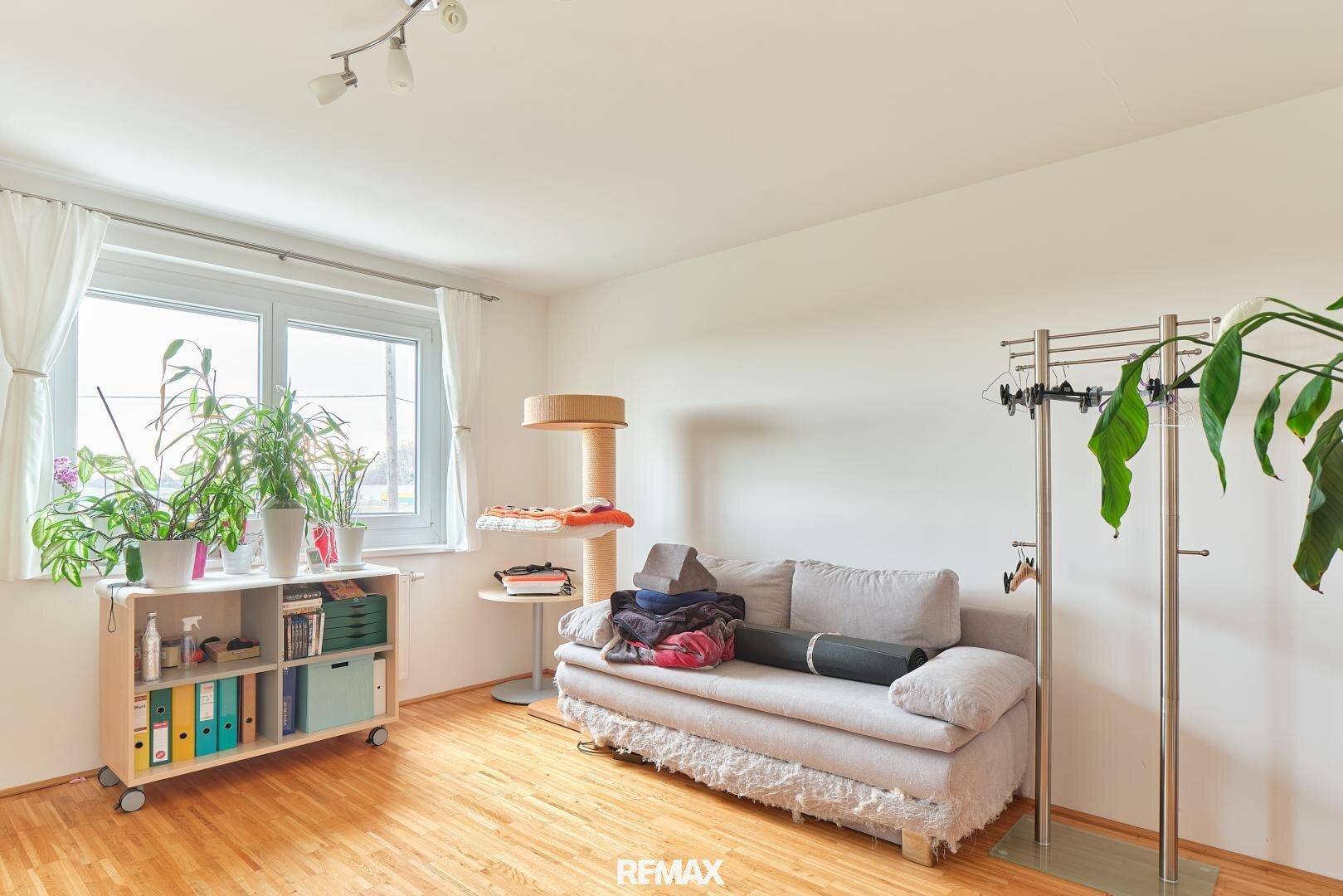 Helles Schlafzimmer mit Fenster, Holzboden und gemütlichem Sofa.