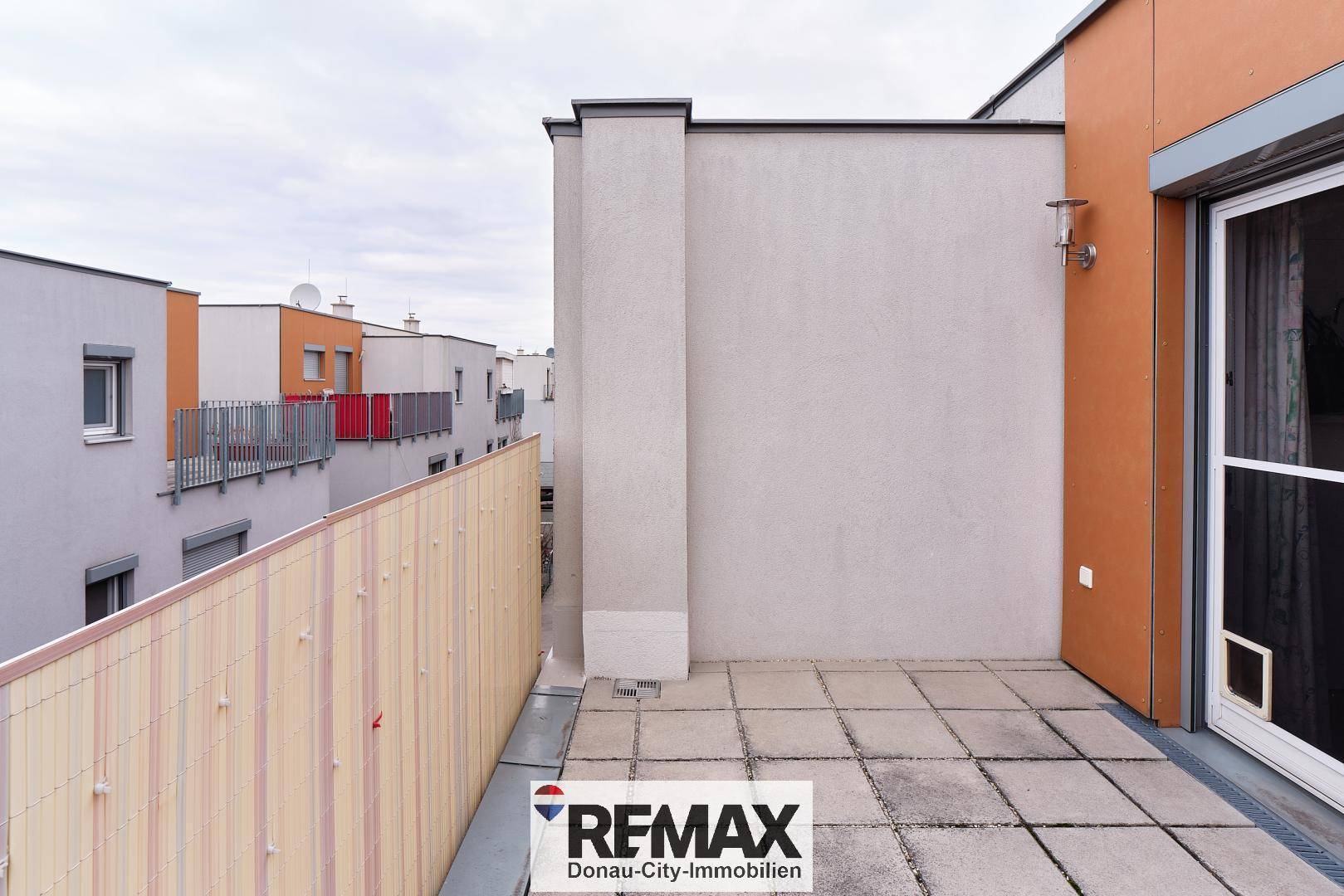 Geräumige Terrasse mit Fliesenboden und Sichtschutz in einer Wohnsiedlung.