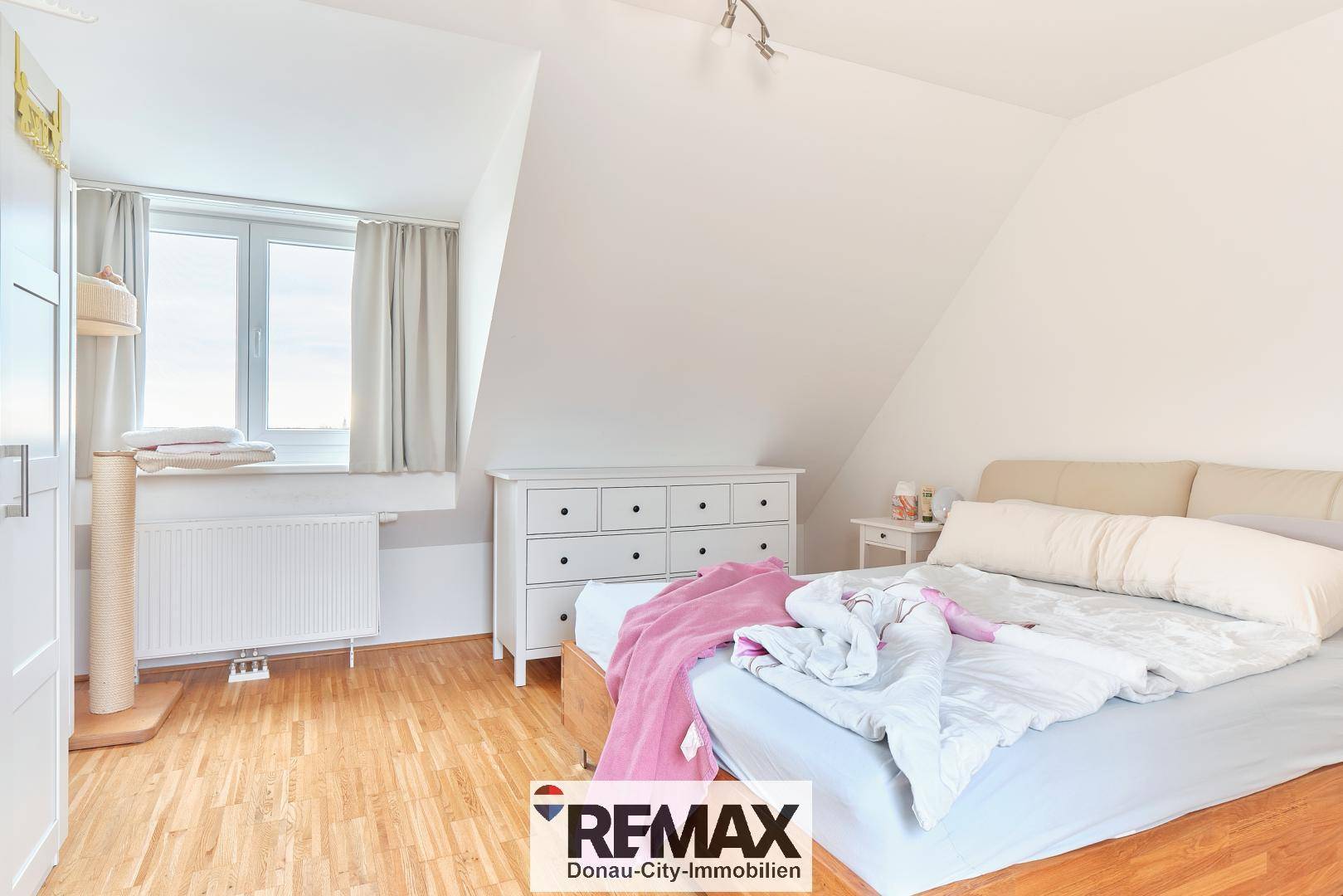 Gemütliches Schlafzimmer im Dachgeschoss mit Fenster, Holzboden und Kommode.