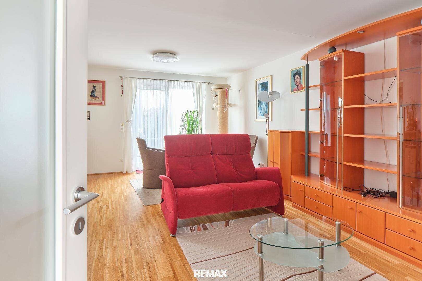 Gemütliches Wohnzimmer mit rotem Sofa, Holzboden und Zugang zu einem hellen Essbereich.