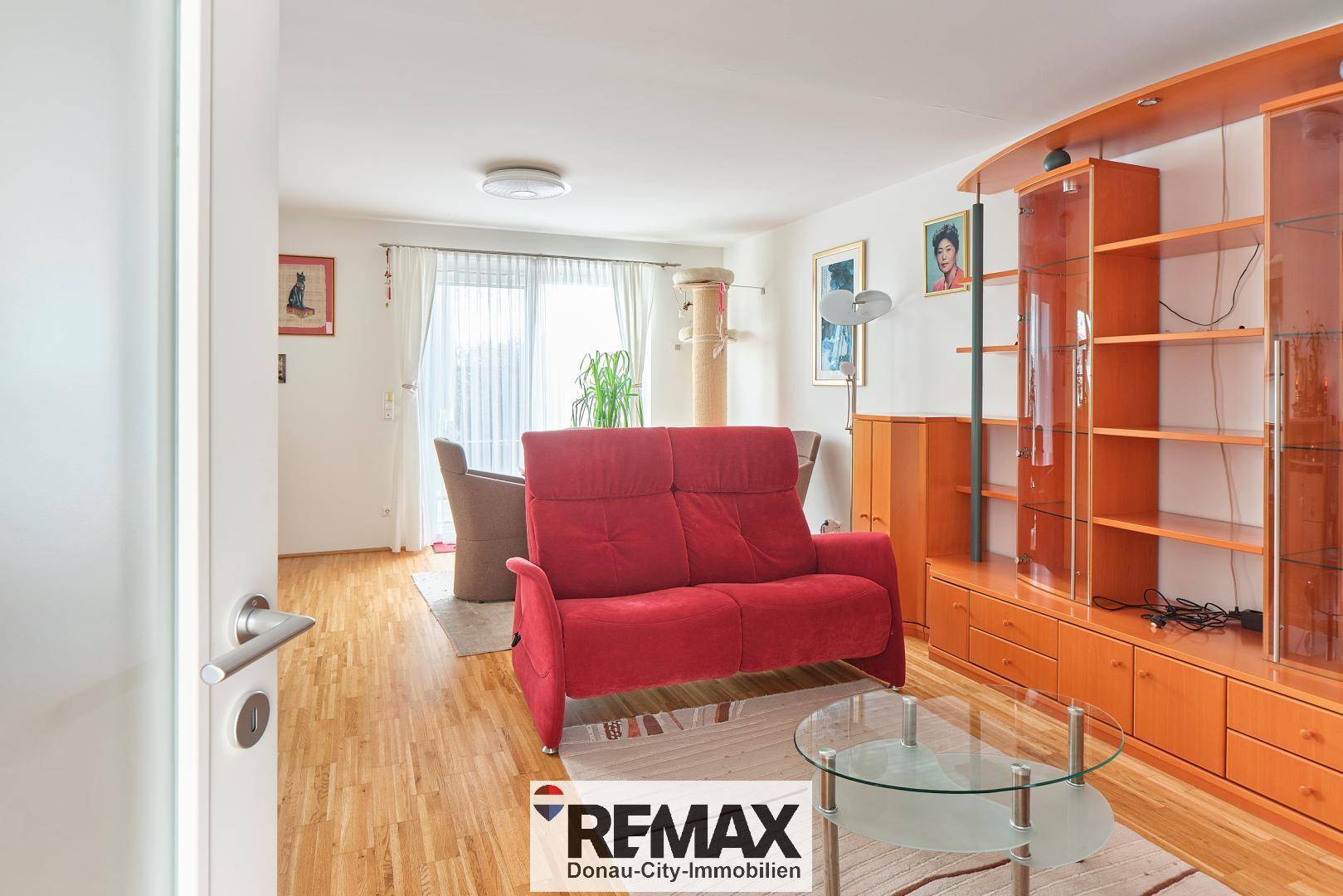 Gemütlicher Wohnbereich mit rotem Sofa, Holzboden und Zugang zum Außenbereich.