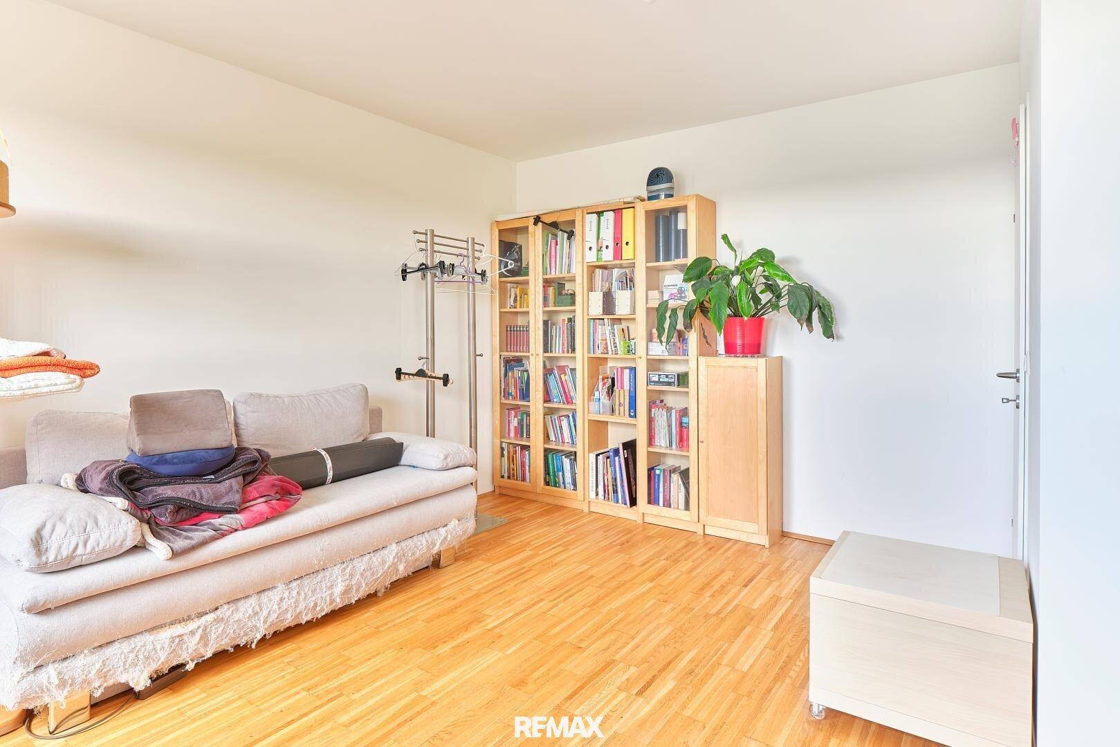 Geräumiges Schlafzimmer mit Holzboden, Bücherregal und hellem Sofa.