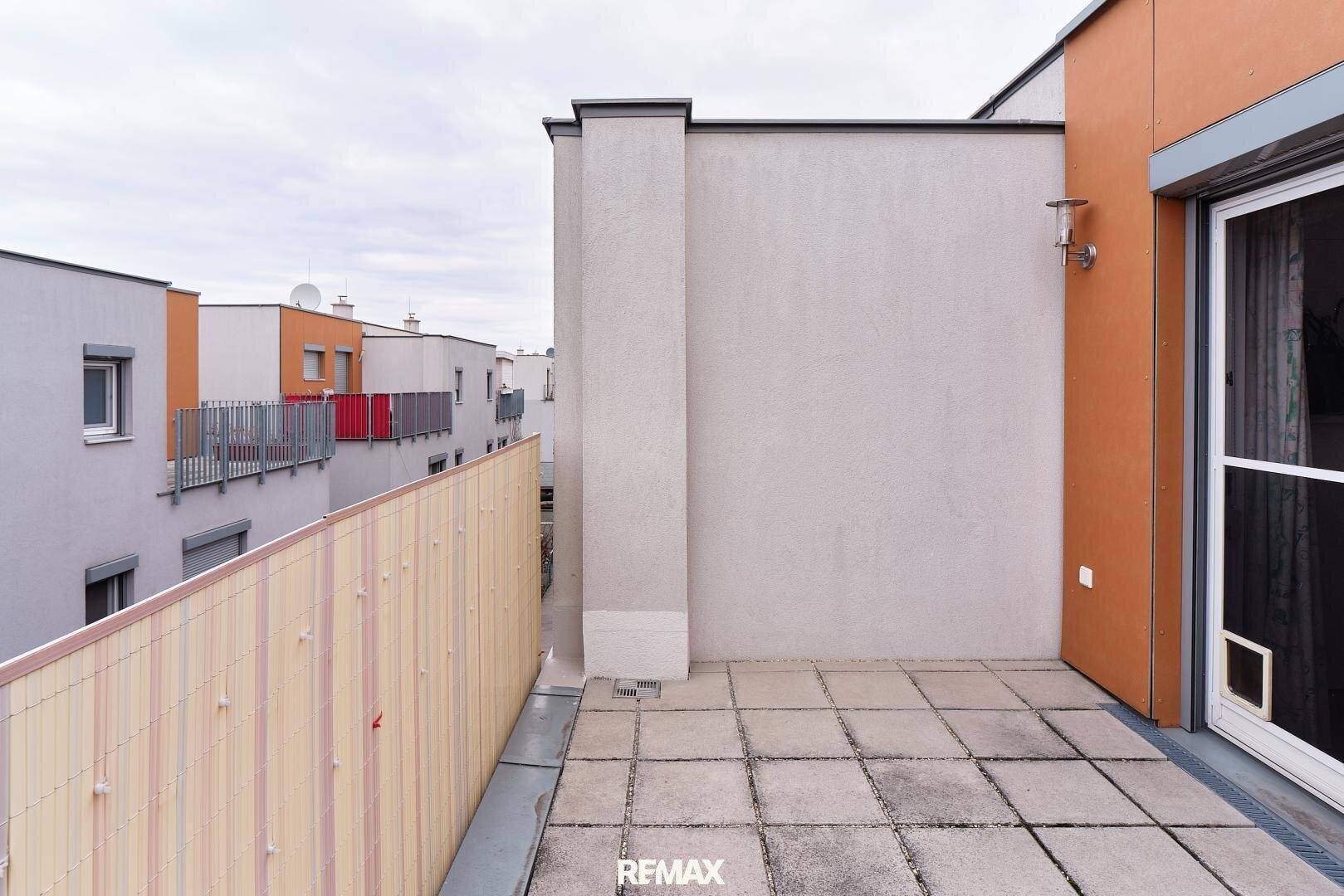 Geräumige Terrasse mit Fliesenboden und Sichtschutz, umgeben von anderen Gebäuden.