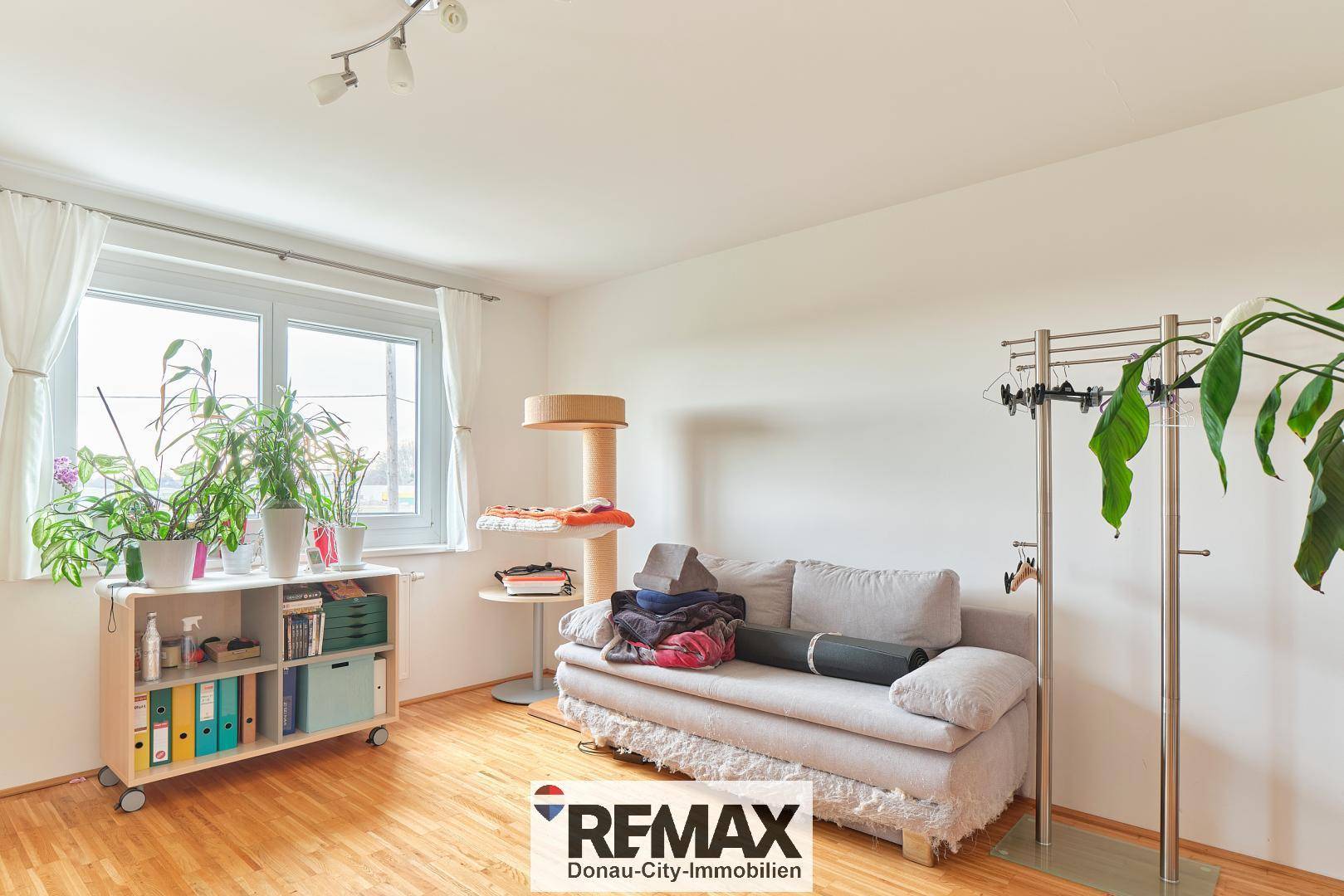 Helles Schlafzimmer mit Holzboden, Fenster und gemütlichem Sofa.