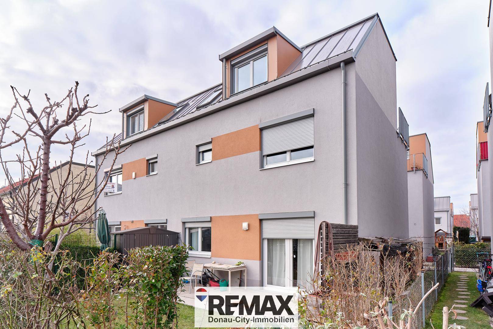 Moderne Reihenhausfassade mit Rollläden und Dachgauben in einer Wohnsiedlung.