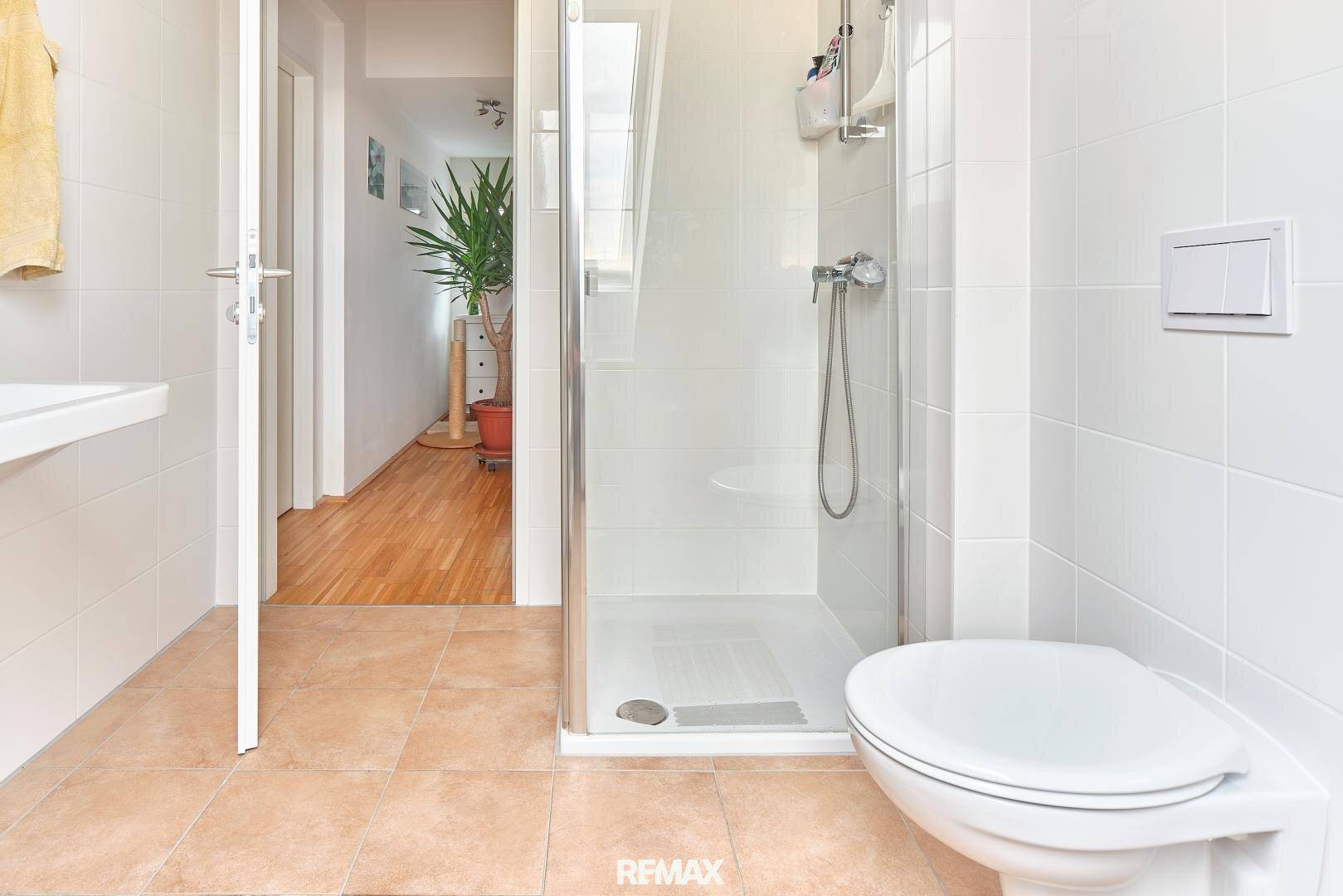Funktionales Badezimmer mit Duschkabine und WC, mit Blick in den Flur.