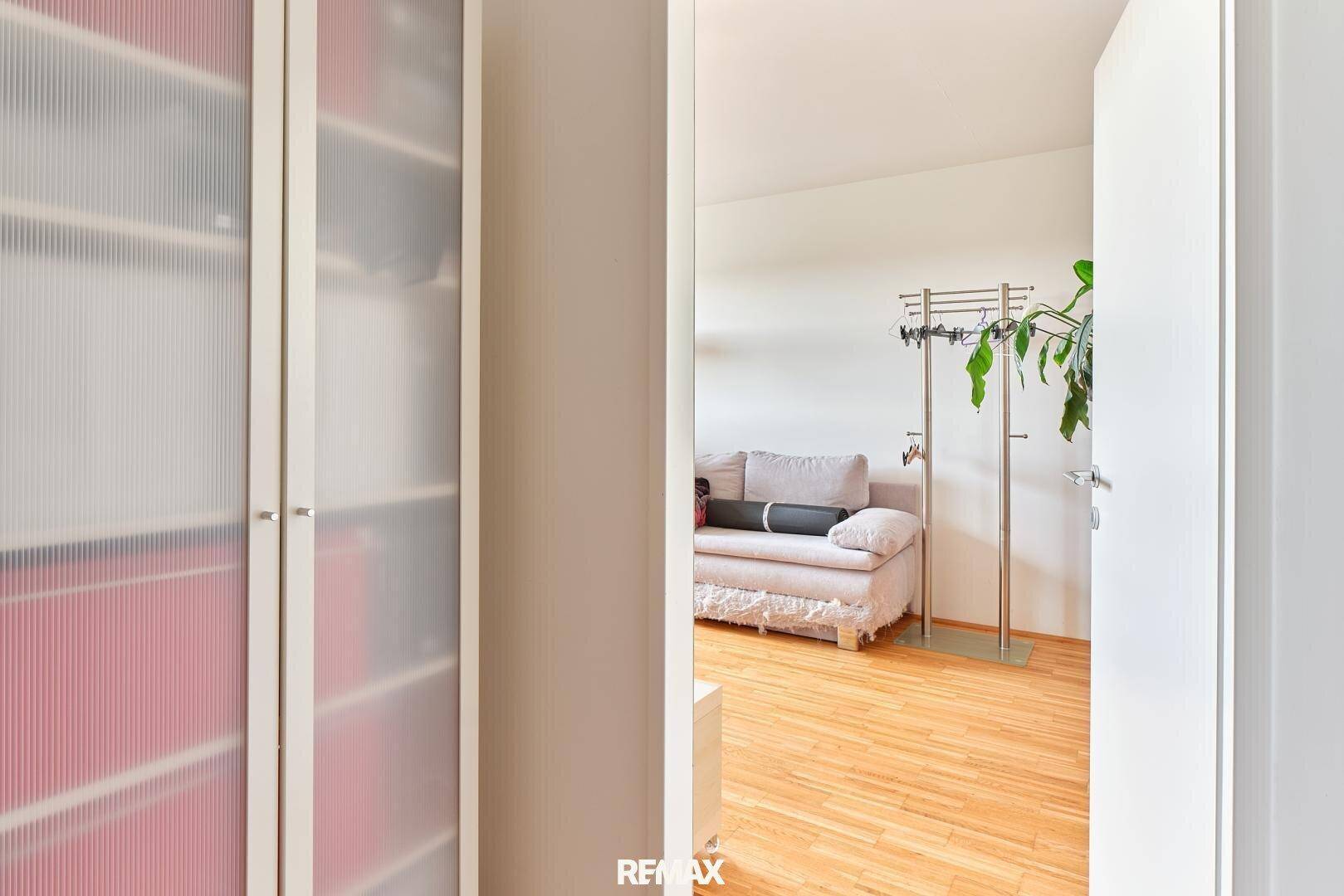 Schlafzimmer mit hellem Sofa, Holzboden und Schrank mit Milchglasfronten.