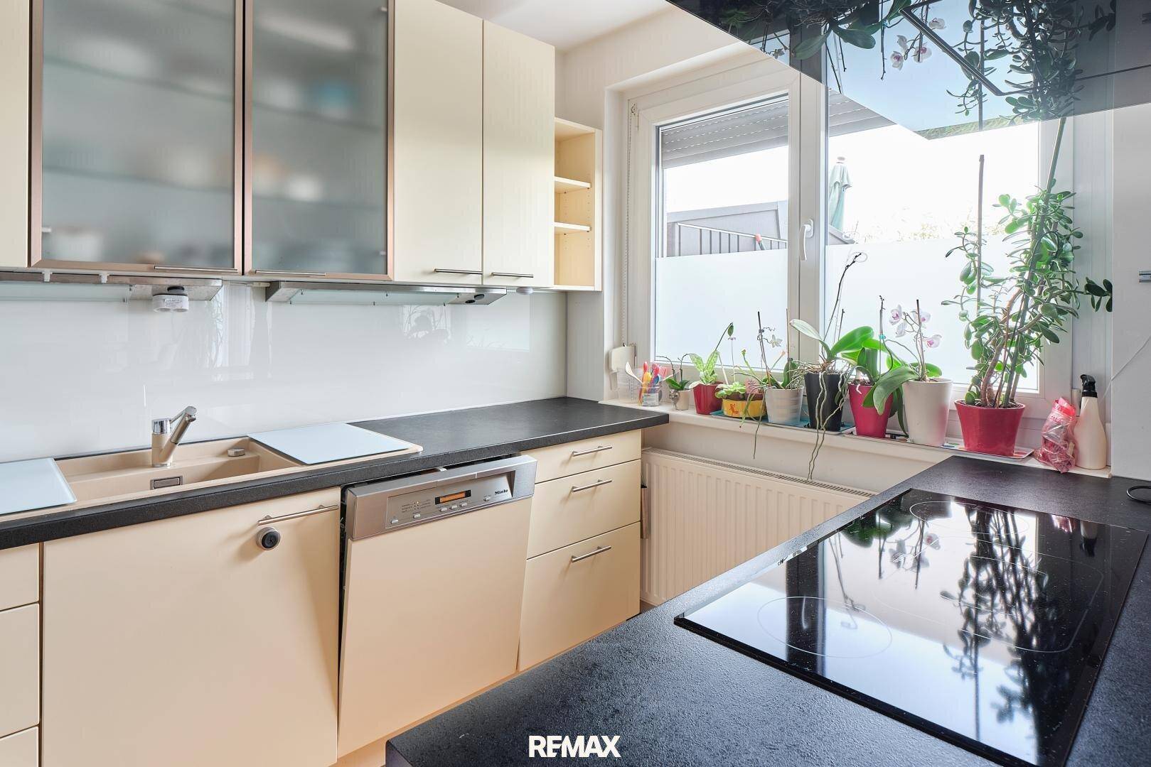 Helle Küche mit Spüle unter dem Fenster, Induktionskochfeld und beigen Schränken.