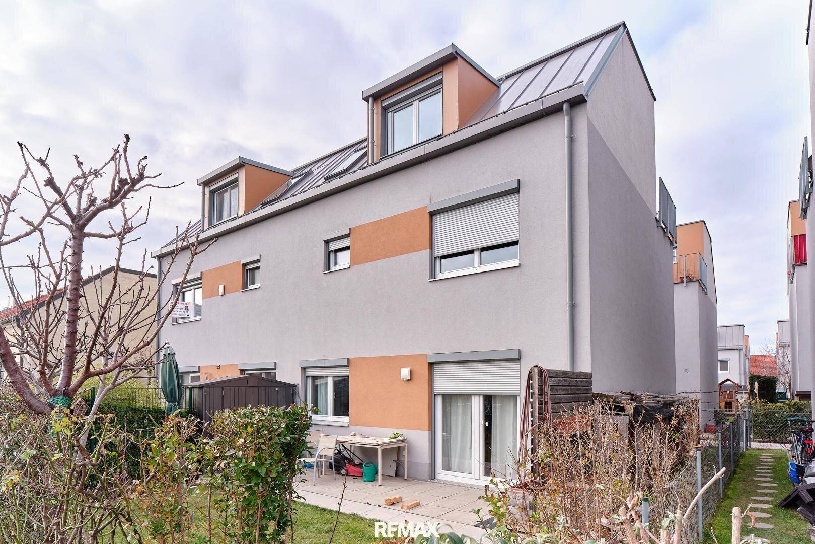 Rückansicht eines Reihenhauses mit Terrasse, Garten und modernen Fenstern.